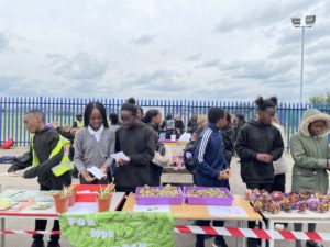 Group of 6 secondary school students sell hand made projects on school playground. The students are handling money and have made an upcycled sign for their business.